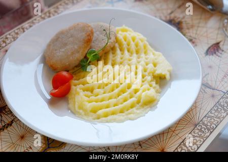 Gebratenes Schnitzel mit Kartoffelpüree und roter frischer Tomate auf dem weißen Teller Stockfoto