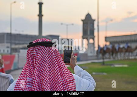 Eindrücke aus Doha/Katar am 7.. Dezember 2022. Arabischer Mann mit traditionellem Kufiya-Film mit Smartphone Kamelreiter, Weltmeisterschaft 2022 in Katar ab 20,11. - 18.12.2022? Stockfoto