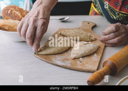 Baker auf dem Tisch bereitet Kuchen zu, die von oben in die Bäckerei gestopft sind. Oma ist in der Küche und backt Kuchen. Stockfoto