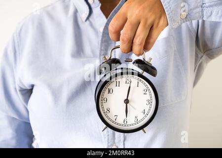 Die Hand einer Frau in Bürokleidung hält um sechs Uhr morgens einen Wecker Stockfoto