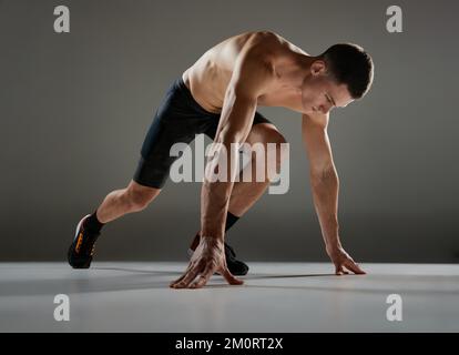 Sportlicher Mann, Muskelsportler, Läufer, der Fahrradshorts in Bewegung und Action trägt, isoliert auf grauem Hintergrund. Energie, Geschwindigkeit, Sport und Schönheit Stockfoto