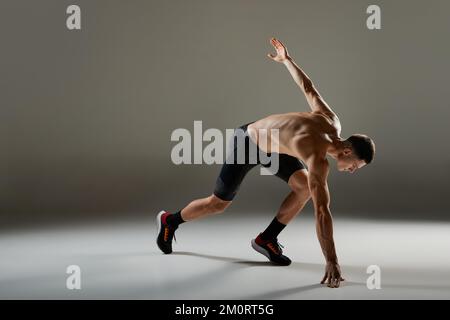 Sportlicher Mann, Muskelsportler, Läufer, der Fahrradshorts in Bewegung und Action trägt, isoliert auf grauem Hintergrund. Energie, Geschwindigkeit, Sport und Schönheit Stockfoto