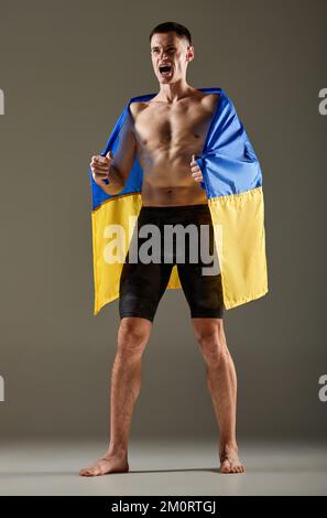 Porträt eines jungen Sportlers, der mit der ukrainischen Flagge auf den Schultern steht und die Emotionen der Sieger ausdrückt. Sieg, Erfolg, Sport, Erfolge Stockfoto
