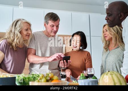 Senior man looking for recipes on smart phone while gathered with friends Stockfoto
