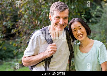 Middle-aged diverse couple looking at camera while hiking out in the woods Stockfoto