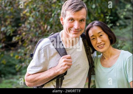 Middle-aged diverse couple looking at camera while hiking out in the woods Stockfoto
