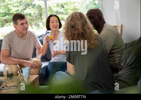 Eine Gruppe verschiedener männlicher und weiblicher Freunde, die im Wohnzimmer sitzen und ihre Unterhaltung genießen Stockfoto