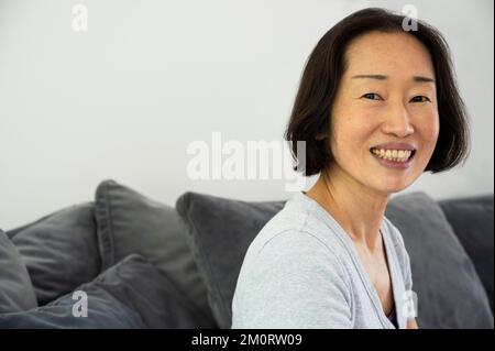 Portrait of Asian-American senior woman smiling and looking at camera while sitting in living room Stockfoto