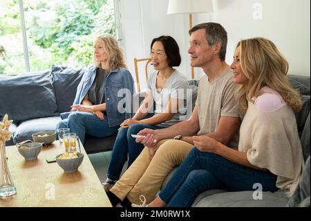 Diverse group of friends sitting on couch watching TV Stockfoto