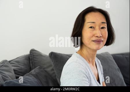Portrait of Asian-American senior woman looking at camera and sitting in living room Stockfoto