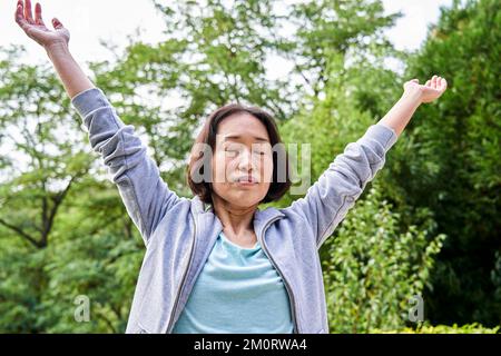 Ältere asiatische Frau, die sich beim Anheben der Arme ausdehnt Stockfoto