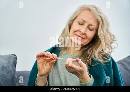 Ältere Frau sitzt auf dem Sofa, während sie Nägel feilt Stockfoto