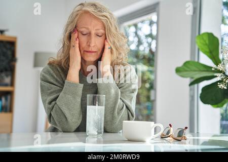 Gestresste Seniorin, die ihr Gesicht berührt, während sie Medizin trinkt Stockfoto