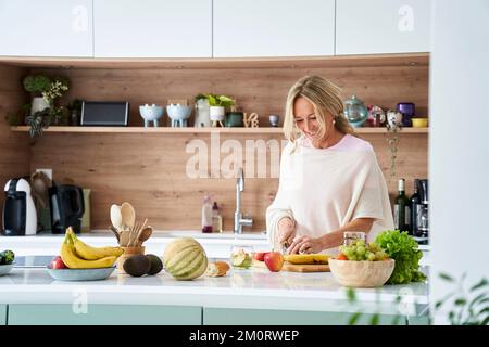 Eine Attratktive Mittelalterin, die in ihrer Küche Obst schneidet Stockfoto