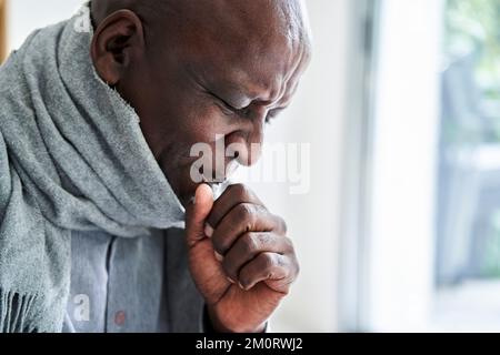 Senior African-American man wearing a scarf and coughing in his hand Stockfoto