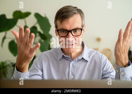 Leitender Mann, der ein Online-Meeting auf dem Laptop führt, während er zu Hause arbeitet Stockfoto