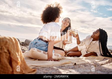 Drei junge, gemischte weibliche Freunde hängen rum und trinken Wein am Strand. Hispanische Frauen trinken draußen ein Glas Wein Stockfoto