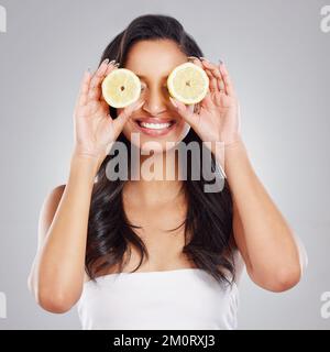 Verwöhnen Sie Ihr Haar mit Naturfreude. Eine attraktive junge Frau mit zwei Zitronenscheiben vor grauem Hintergrund. Stockfoto