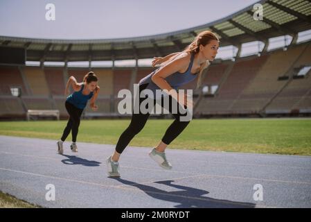 Zwei Freundinnen joggen durch das Stadion, auf einer blauen Sportstrecke und an einem wunderschönen sonnigen Tag Stockfoto