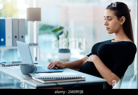 Mit ihren Aufgaben beschäftigt zu sein. Eine schwangere Geschäftsfrau, die an einem Laptop in einem Büro arbeitet. Stockfoto