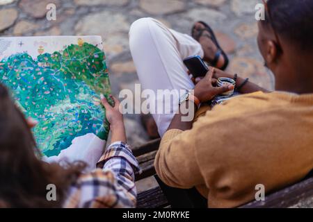 Ein Mann sitzt während einer Pause am Telefon. Seine Freundin sucht auf der Karte nach einem nächsten Reiseziel Stockfoto