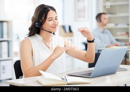 Lassen Sie uns das im Detail besprechen. Eine junge Geschäftsfrau, die ein Headset trägt, während sie mit einem Laptop im Büro ein Videogespräch führt. Stockfoto
