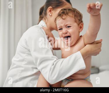 Wir sind fast fertig. Ein kleines Baby, das weint, während es von einem Arzt untersucht wird. Stockfoto