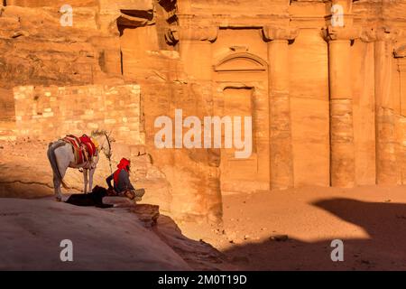 Petra, Jordanien - 3. November 2022: Beduinenmensch, Hund und Esel und Blick auf das Kloster Ad Deir in der antiken Stadt, Panoramablick bei Sonnenuntergang, UNESCO World He Stockfoto