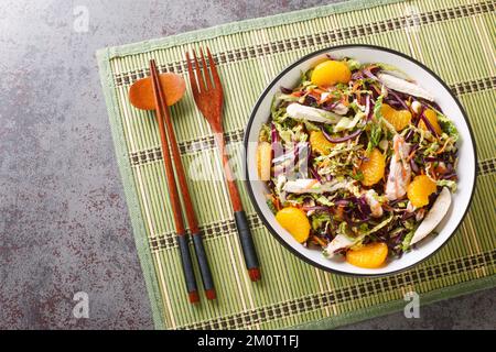 Amerikanischer chinesischer Mandarin-Hähnchensalat mit Gemüse, Kräutern und Nudeln in Nahaufnahme auf einem Teller auf dem Tisch. Horizontale Draufsicht von oben Stockfoto