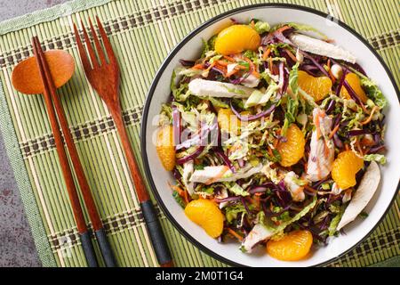 Chinesischer Hähnchensalat mit Mandarin, Kohl, Karotten, grünen Zwiebeln und Hähnchen mit asiatischem Dressing aus nächster Nähe in der Schüssel auf dem Tisch. Horizontal Stockfoto