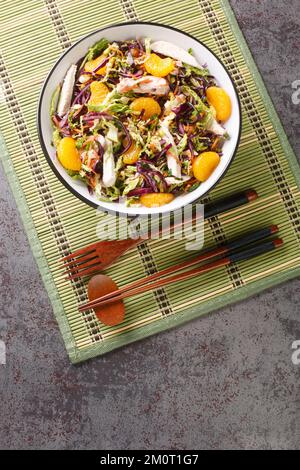 Chinesisch inspirierter Hähnchensalat mit Tangerinen, Rotkohl, Chinakohl, Karotten und Nudeln schließen sich in der Schüssel auf dem Tisch zusammen. Vertikale Draufsicht Stockfoto