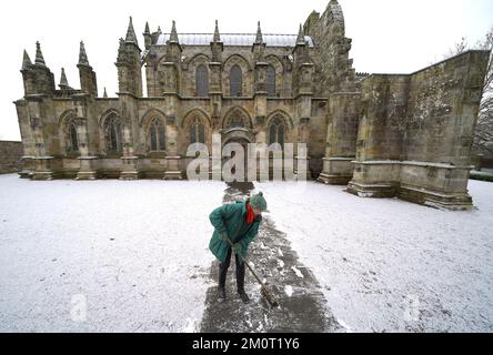 Eine Person räumt den Weg in der Rosslyn Chapel in Edingburgh nach einer leichten Schneeflocke. Foto: Donnerstag, 8. Dezember 2022. Stockfoto