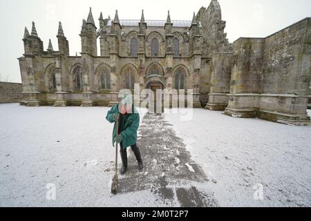 Eine Person räumt den Weg in der Rosslyn Chapel in Edingburgh nach einer leichten Schneeflocke. Foto: Donnerstag, 8. Dezember 2022. Stockfoto