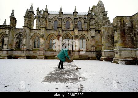 Eine Person räumt den Weg in der Rosslyn Chapel in Edingburgh nach einer leichten Schneeflocke. Foto: Donnerstag, 8. Dezember 2022. Stockfoto