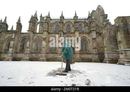 Eine Person räumt den Weg in der Rosslyn Chapel in Edingburgh nach einer leichten Schneeflocke. Foto: Donnerstag, 8. Dezember 2022. Stockfoto