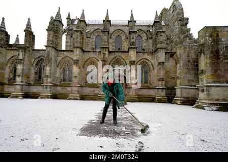 Eine Person räumt den Weg in der Rosslyn Chapel in Edingburgh nach einer leichten Schneeflocke. Foto: Donnerstag, 8. Dezember 2022. Stockfoto