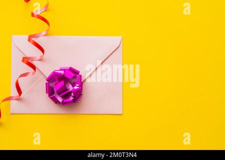 Draufsicht auf Umschlag und Geschenkbogen in der Nähe der Schlangenlinie auf gelbem Hintergrund, Stockbild Stockfoto