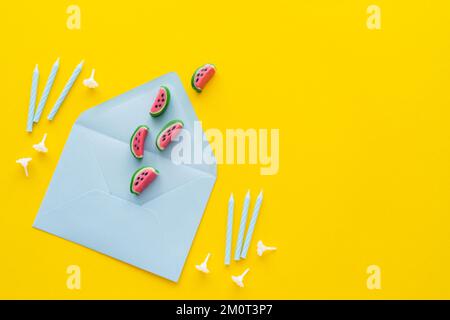 Draufsicht auf Süßigkeiten auf Umschlag in der Nähe festlicher Kerzen auf gelbem Hintergrund, Stockbild Stockfoto