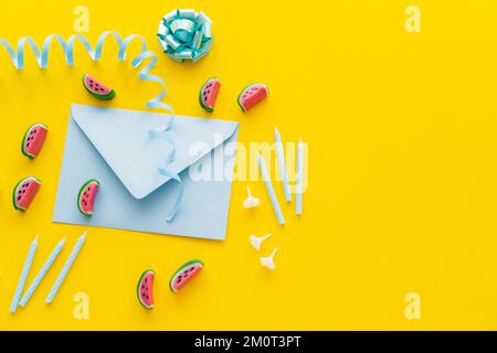 Ansicht von oben mit festlichen Kerzen in der Nähe des Umschlags und Süßigkeiten auf gelbem Hintergrund, Stockbild Stockfoto