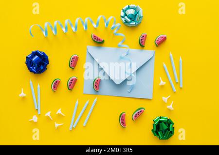 Draufsicht auf festliche Kerzen in der Nähe von Süßigkeiten und Umschlag auf gelbem Hintergrund, Stockbild Stockfoto