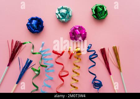 Draufsicht der Geschenkbogen neben Schlangenlinien und Trinkhalmen auf pinkfarbenem Hintergrund, Stockbild Stockfoto