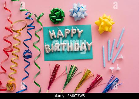 Draufsicht der festlichen Kerzen in Form von Happy Birthday Schriftzug neben Schlangenhaut und Trinkhalmen auf pinkem Hintergrund, Stockbild Stockfoto