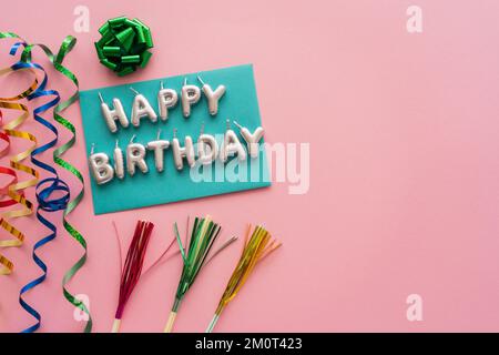 Draufsicht der Kerzen in Form von Happy Birthday Schriftzug neben Schlangenhaut und Trinkhalmen auf rosa Hintergrund, Stockbild Stockfoto