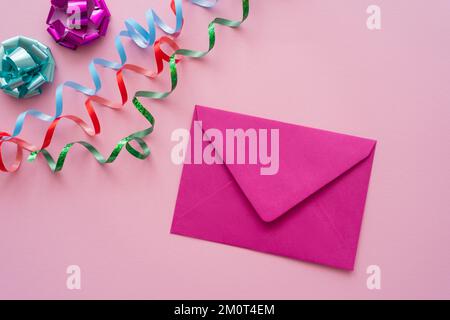 Ansicht des Umschlags von oben in der Nähe von Schlangenlinien und Geschenkbogen auf pinkfarbenem Hintergrund, Stockbild Stockfoto