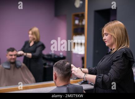 Die Frau schneidet dem Mann die Haare Stockfoto