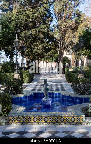 Spanien, Andalusien, Cadiz, Alameda Apodaca, Bronzestatue eines kleinen Jungen in der Mitte eines mit Azuleros geschmückten Brunnens entlang der von Bäumen gesäumten Promenade am Meer Stockfoto