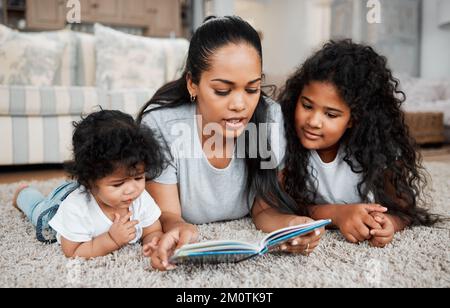 Gemeinsam Traumwelten erkunden. Eine Mutter, die ihren Töchtern vorliest. Stockfoto