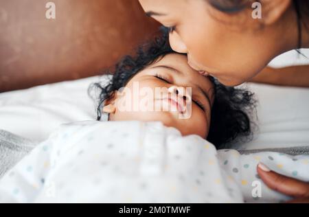 Ich hoffe, sie lässt mich sie immer küssen. Eine Frau küsst ihr schlafendes Baby auf die Stirn. Stockfoto