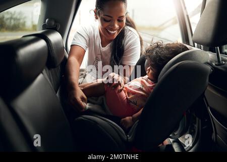 Fahrgeschäfte beruhigen sie immer. Eine Frau, die ihr Baby in ihren Autositz setzt. Stockfoto