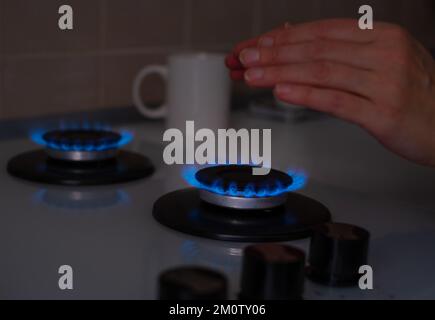 Eine Frau wärmt ihre Hände in der Nähe des Gases in der Küche. Niedrige Temperatur im Zimmer, steigende Preise für Heizung, kalt im Apartment-Konzept. Energiekarzinom Stockfoto